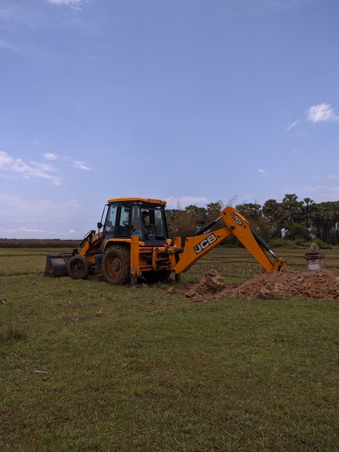 Excavator working with dirt in open grassy field under clear blue sky. Ideal for construction themes.
